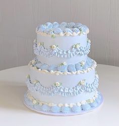 a three tiered blue and white wedding cake with flowers on the top, sitting on a table