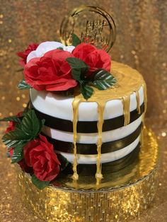 a black and white striped cake with red flowers on top, dripping gold icing