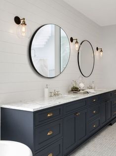 two sinks and mirrors in a bathroom with white tile flooring, blue cabinets and gold pulls