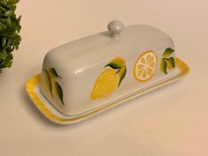 a ceramic dish with lemons and leaves painted on the side, sitting next to a potted plant