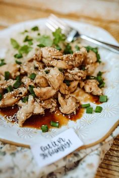 a white plate topped with meat covered in gravy and garnished with green onions