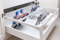 two pairs of shoes are in the bottom drawer of a white shoe cabinet with drawers