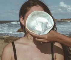 a woman holding up a white frisbee in front of her face on the beach