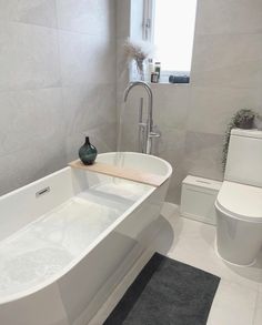 a white bathtub sitting next to a toilet in a bathroom with a black rug on the floor