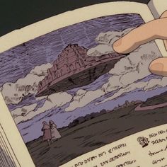 a hand is holding an open book in front of a cartoon scene with clouds and a castle