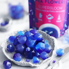 blue glass beads in a white bowl next to a bottle of tea flower's