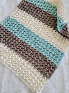 a crocheted blanket laying on top of a bed next to a white pillow