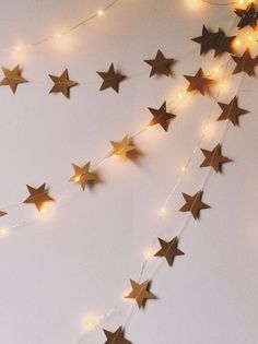 a string of gold stars hanging from the ceiling next to a white wall with lights on it