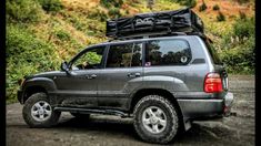 a grey suv parked on top of a dirt road next to a lush green hillside