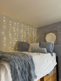 a white bed topped with lots of pillows next to a wall covered in string lights