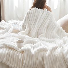 a woman wrapped in a white blanket sitting on top of a bed