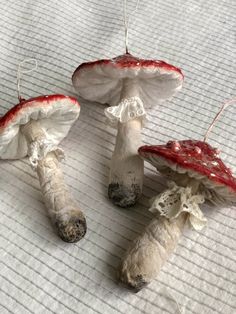 three white mushrooms with red tops sitting on a sheet