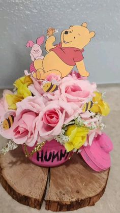 a winnie the pooh centerpiece with flowers and bees is on top of a piece of wood