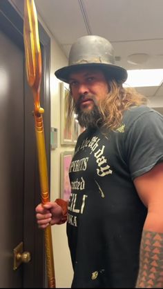 a man with long hair wearing a hat and holding a large metal stick in his hand