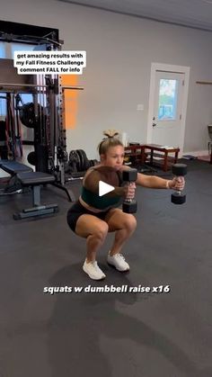 a woman squatting down while holding a dumbbell in a gym with other equipment behind her