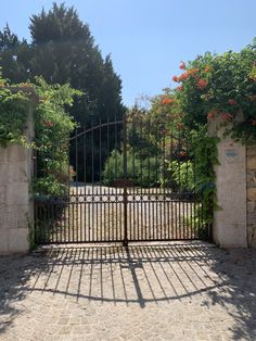 an iron gate with flowers growing over it and a stone walkway leading to the entrance