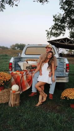 a man and woman sitting in the back of a pick up truck next to pumpkins