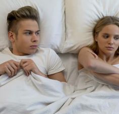 a man and woman laying in bed with white sheets on their sides looking at each other