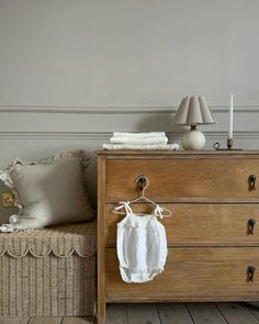 a baby's shirt hanging on a clothes rail in front of a dresser with white pillows