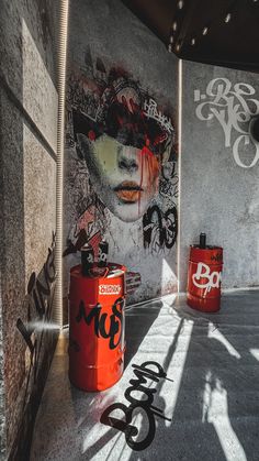 graffiti is painted on the wall next to two red trash cans in an empty room