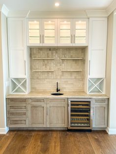 an empty kitchen with white cabinets and wood flooring is pictured in this image, there is a wine cooler on the counter