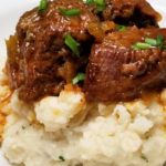 meat and gravy on top of mashed cauliflower in a white bowl