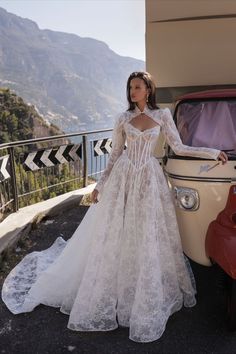 a woman standing next to an old car wearing a wedding dress with long sleeves and open back