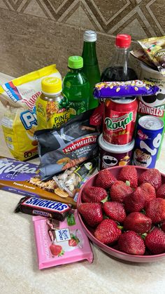 a bowl full of strawberries next to some snacks and drinks on a counter top