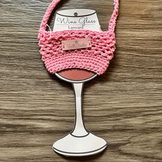 a pink crocheted wine glass holder on a wooden table next to a bottle opener