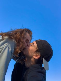 a man and woman kissing each other in front of a blue sky with no clouds