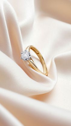 an engagement ring on top of a white satin fabric with a diamond in the center