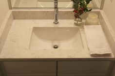 a bathroom sink sitting under a mirror next to a vase with flowers on top of it