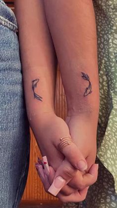 two people holding hands with small tattoos on their arms and wrist, both showing arrows