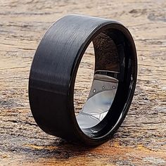 a black ceramic ring with silver inlays sits on a stone surface and looks like it is made out of wood