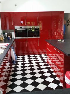 a kitchen with black and white checkered flooring, red cabinets, and stainless steel appliances