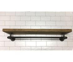 a wooden shelf mounted to the side of a white tiled wall next to a black pipe