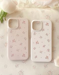 two iphone cases sitting on top of a table next to a flowery rose bouquet