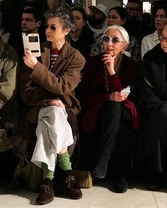 two women sitting next to each other in front of a group of people with cell phones