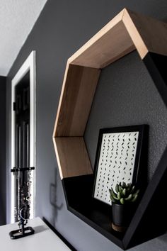 a black and white wall with a wooden hexagonal shelf next to a potted plant