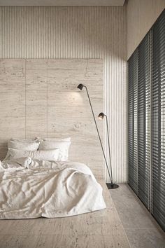 a bed with white sheets and pillows in a room next to a wall mounted lamp