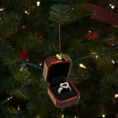 an ornament hanging from a christmas tree with a ring inside it and lights on