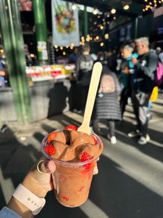 a person holding up a cup with ice cream and strawberries in it on the street