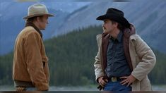 two men standing next to each other with mountains in the background