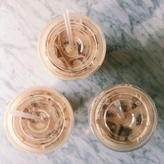 three iced drinks sitting on top of a marble table next to each other with straws in them