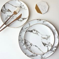 two marble plates with gold rims and one has a fork on the plate next to it