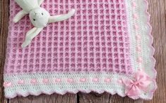 a pink and white blanket with a stuffed animal on it, sitting on a wooden surface