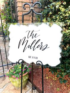 a white sign that says the miles on it next to some plants and flowers in front of a brick building