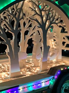 a white paper cut out of trees with lights around it and some people in the background