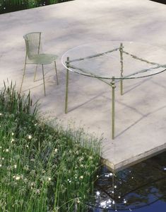 a glass table and two chairs sitting on the edge of a pond