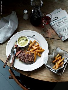 a steak and french fries on a white plate next to a glass of red wine